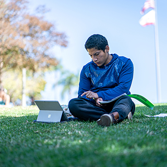 student studying with laptop in grass